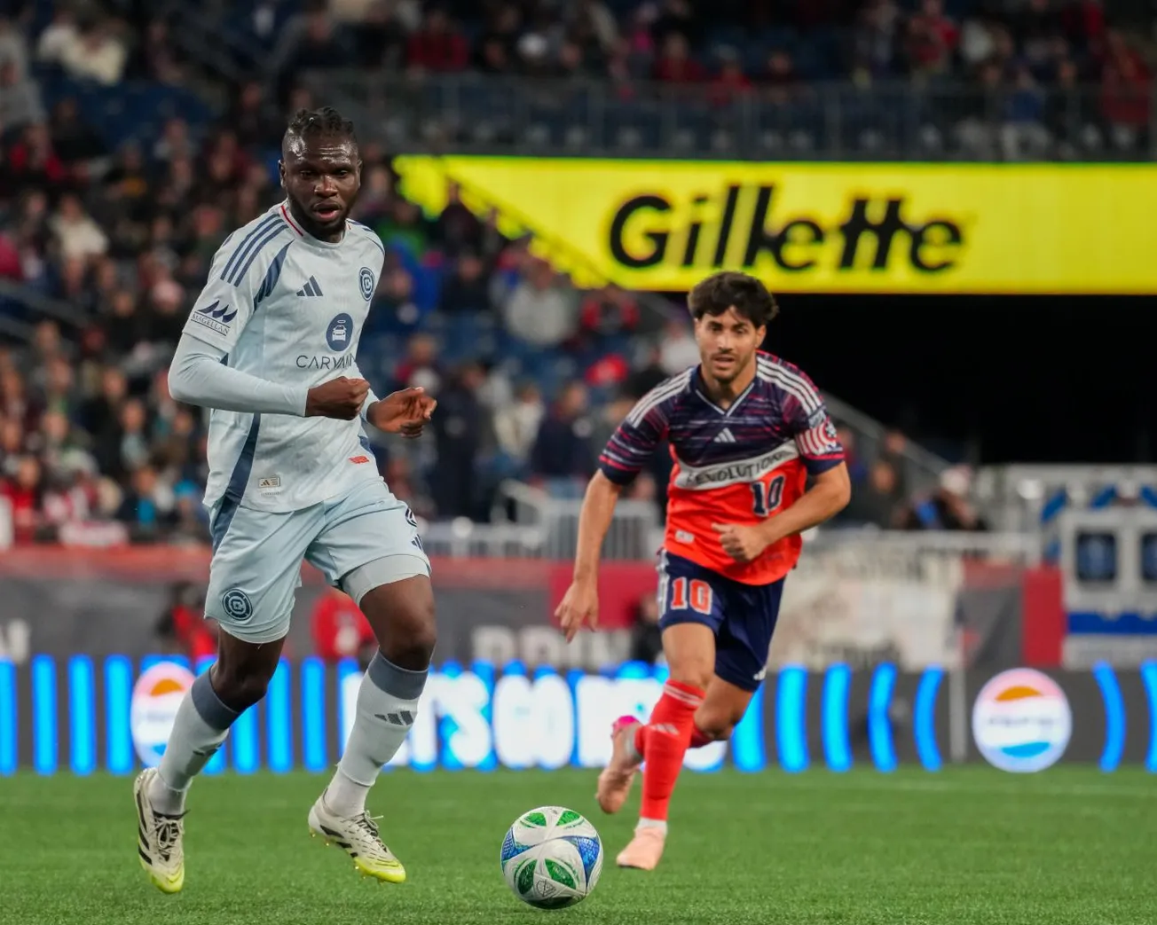 Rominigue Kouamé plays the ball forward against Carles Gil during the Chicago Fire's game against the New England Revolution