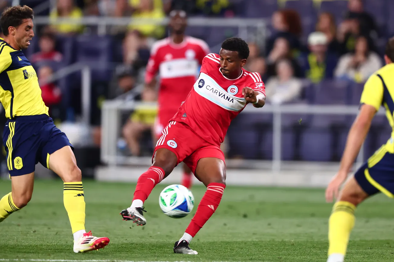 Three soccer players - two from Nashville SC in yellow jerseys, and Maren Haile-Selassie from the Chicago Fire n red kicking the ball